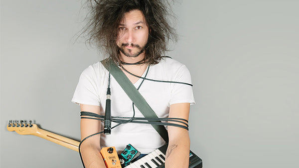messy looking musician wrapped in guitar cables, guitar, keyboard and guitar pedals