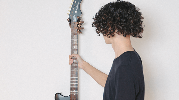 teenage with black curly hair reaching for guitar hanging on wall.