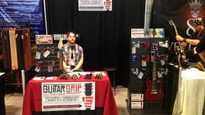 man behind guitar wall hanger booth at the NAMM trade show.