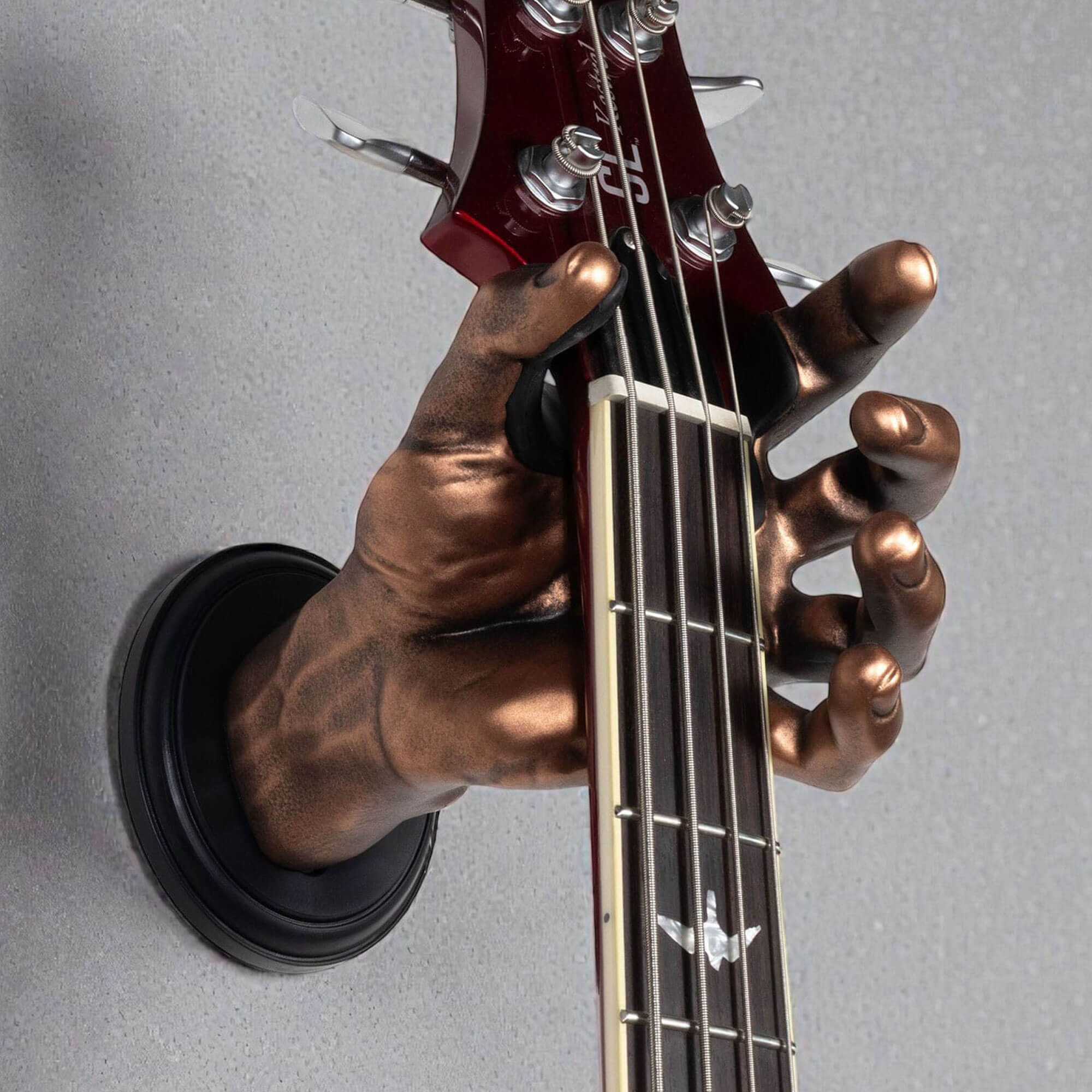 Antique copper hand-shaped guitar wall mount holding bass guitar headstock, close-up detail of GuitarGrip hanger