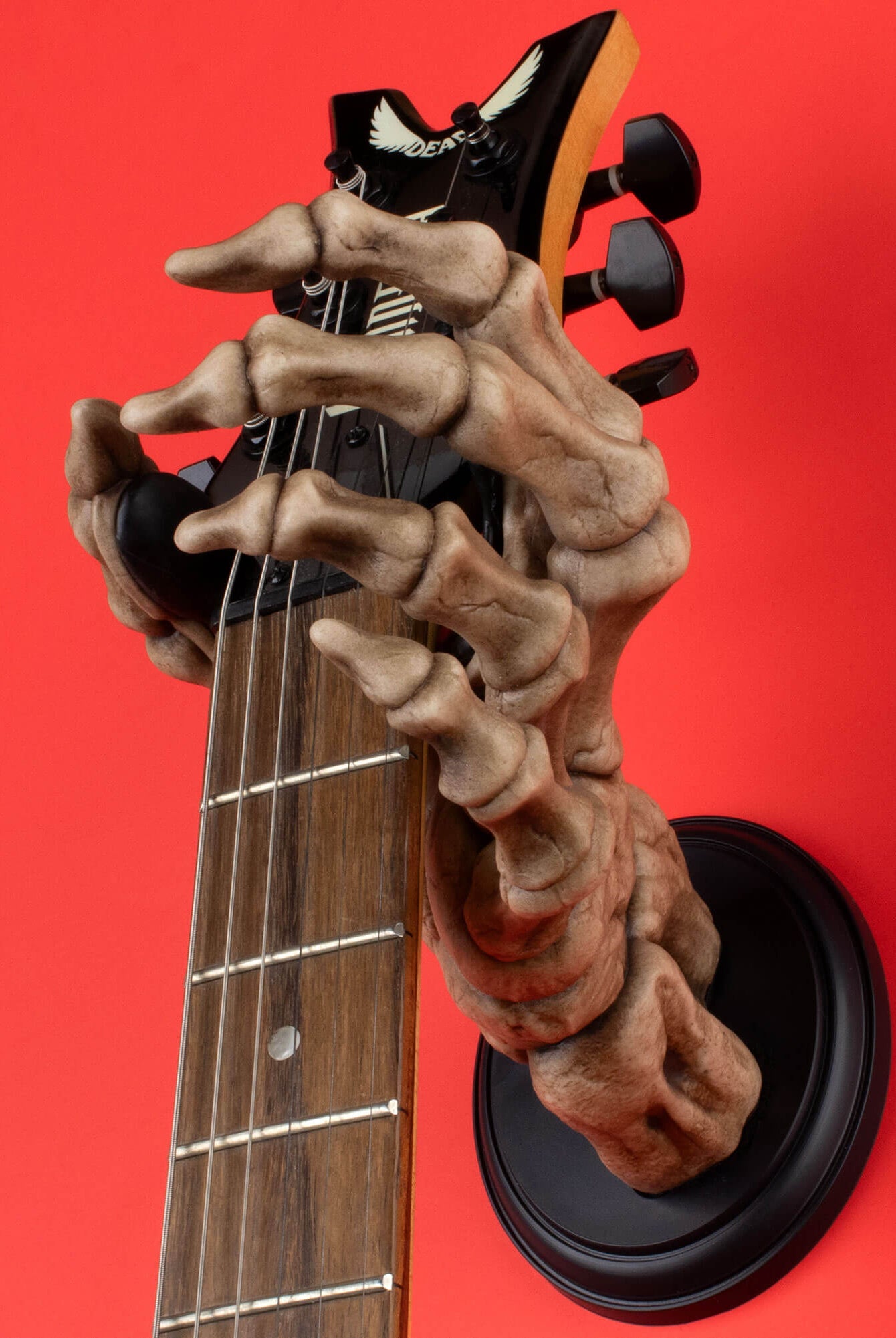 Skeleton hand wall mount on red background holding electric guitar.