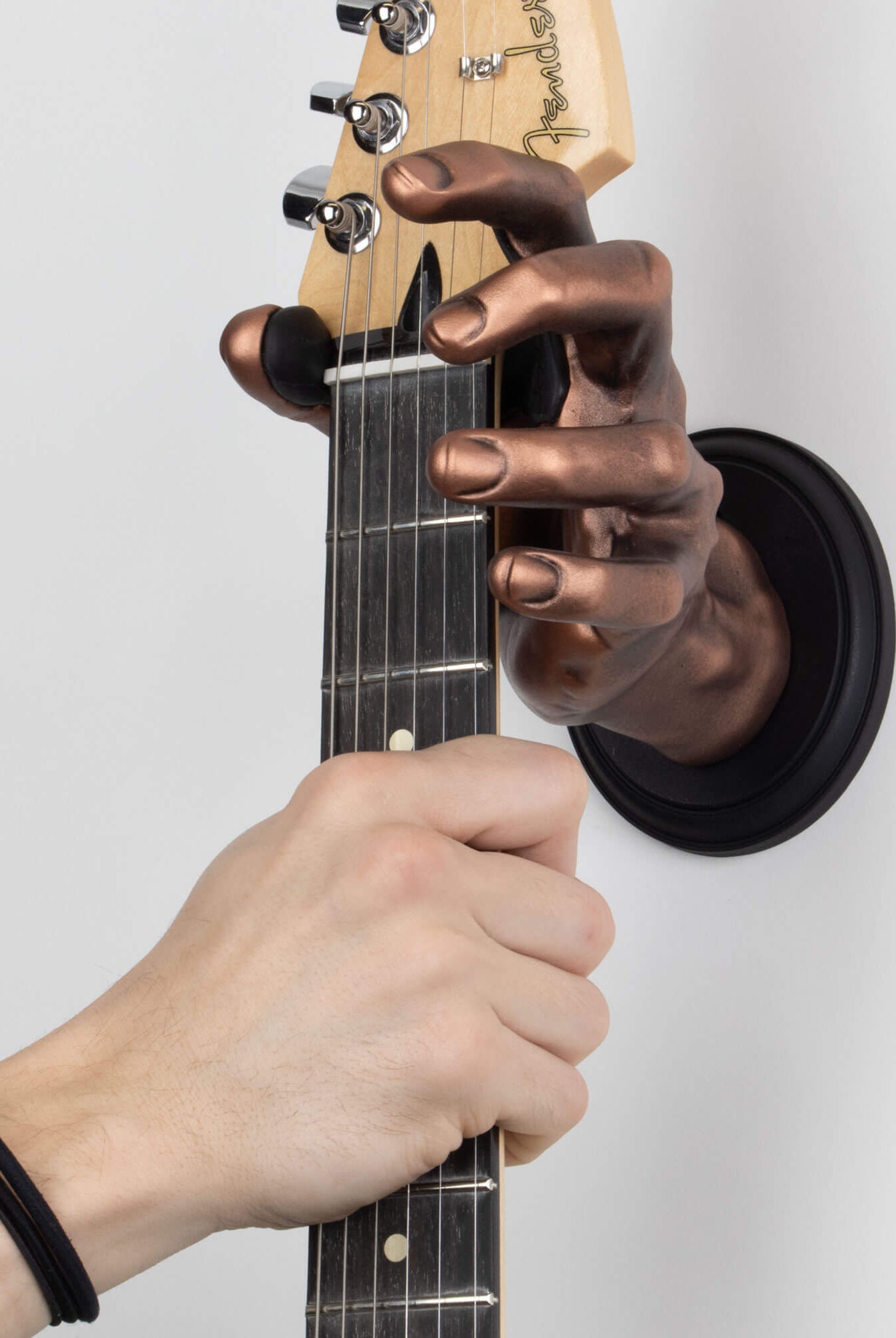 Copper guitar hanger wall mount shaped like a hand on white background.