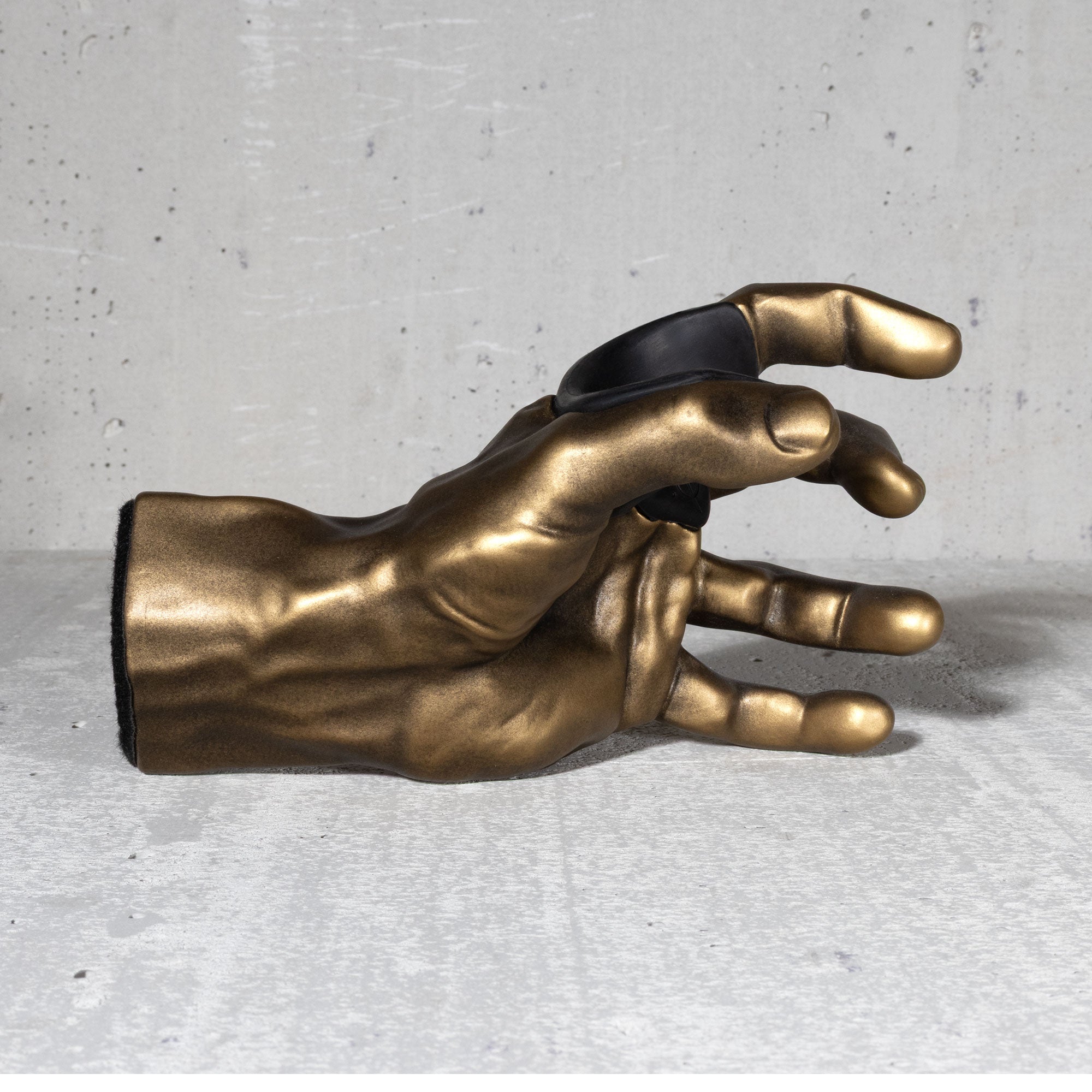 Gold hand sculpture guitar hanger with black padded insert against a gray concrete background