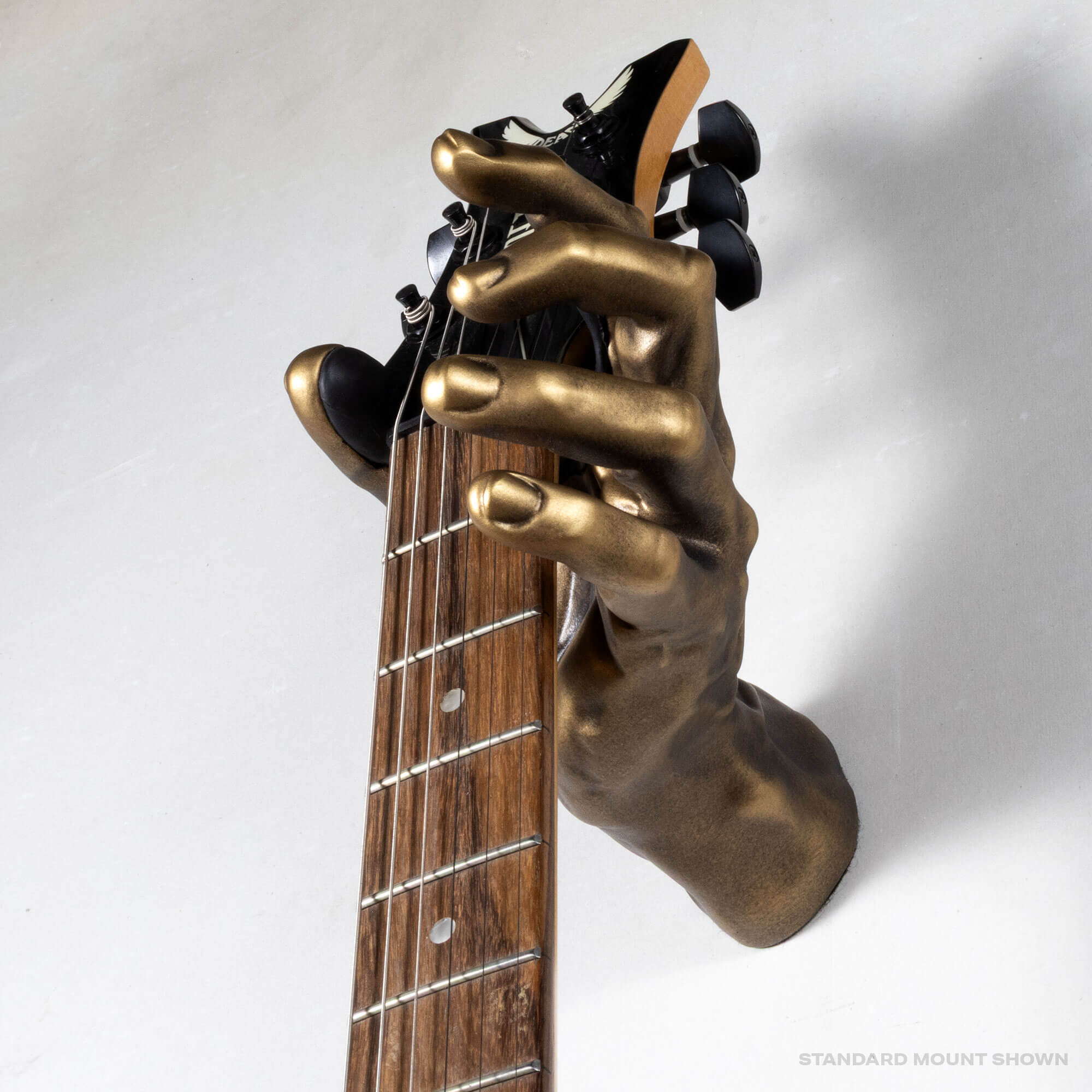 Antique bronze hand-shaped guitar wall mount holding bass guitar headstock, close-up detail of GuitarGrip hanger.