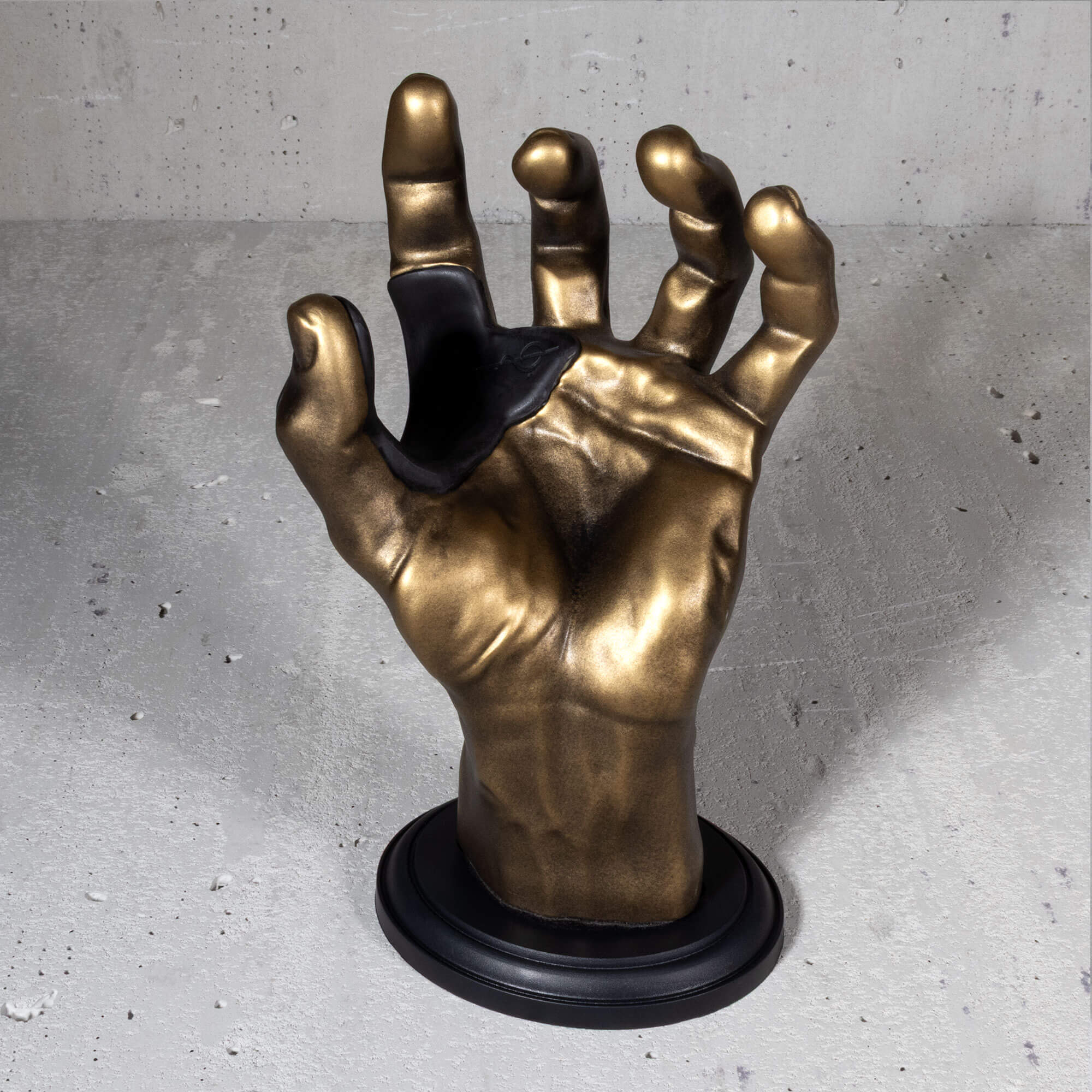 Hand guitar hanger in gold finish on grey wall.