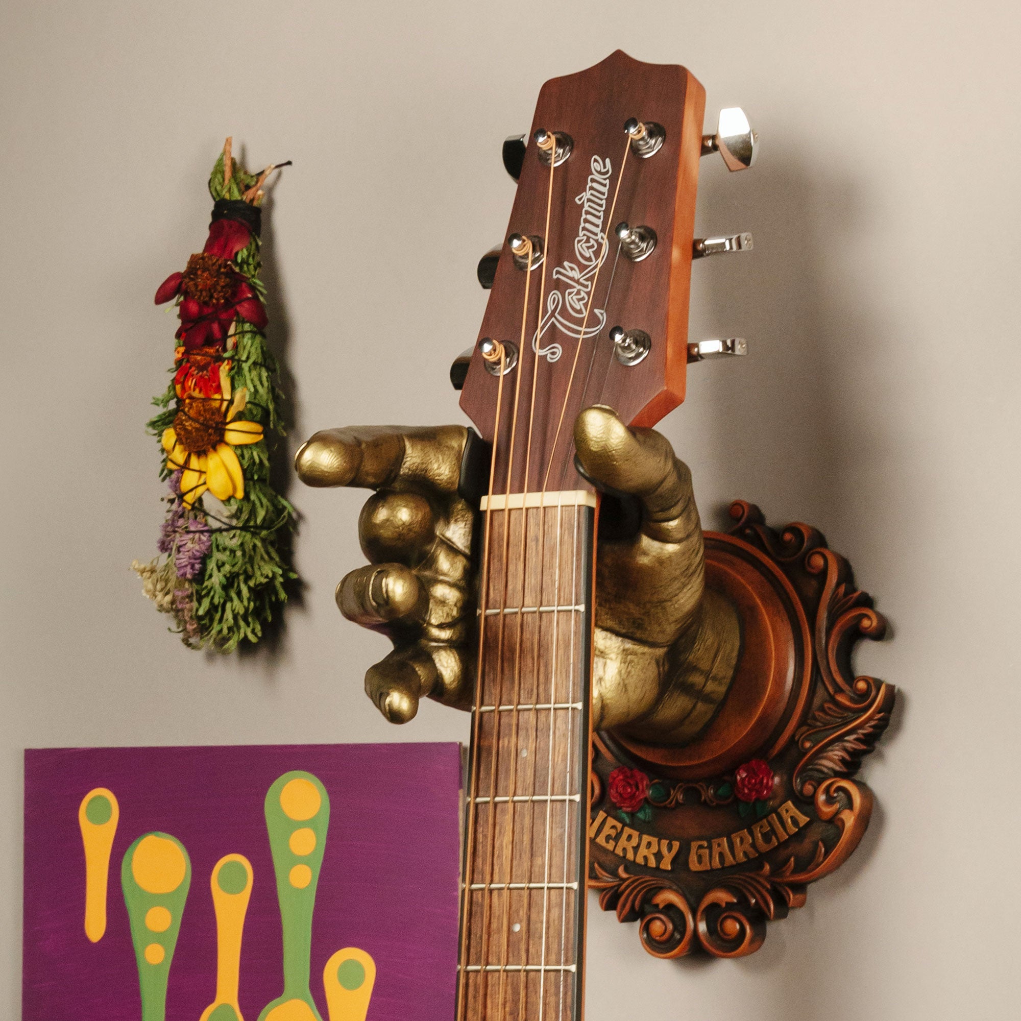 Jerry Garcia Officially Licensed Guitar Hanger from GuitarGrip. On wall with purple artwork and sage.