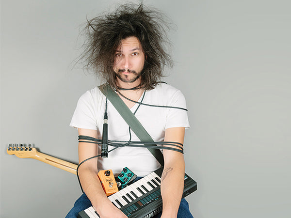 messy looking musician wrapped in guitar cables, guitar, keyboard and guitar pedals