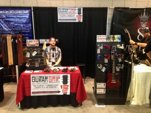 man behind guitar wall hanger booth at the NAMM trade show. 