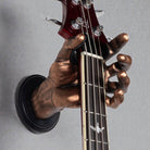 Antique copper hand-shaped guitar wall mount holding bass guitar headstock, close-up detail of GuitarGrip hanger