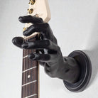 Wall guitar hanger shaped like a hand, black in color and holding a fender Stratocaster against a off white wall.