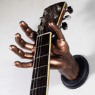 Copper acoustic guitar hanger in the shape of a hand on a white backkground.