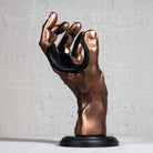 Copper guitar hanger in the shape of a hand on a grey background.