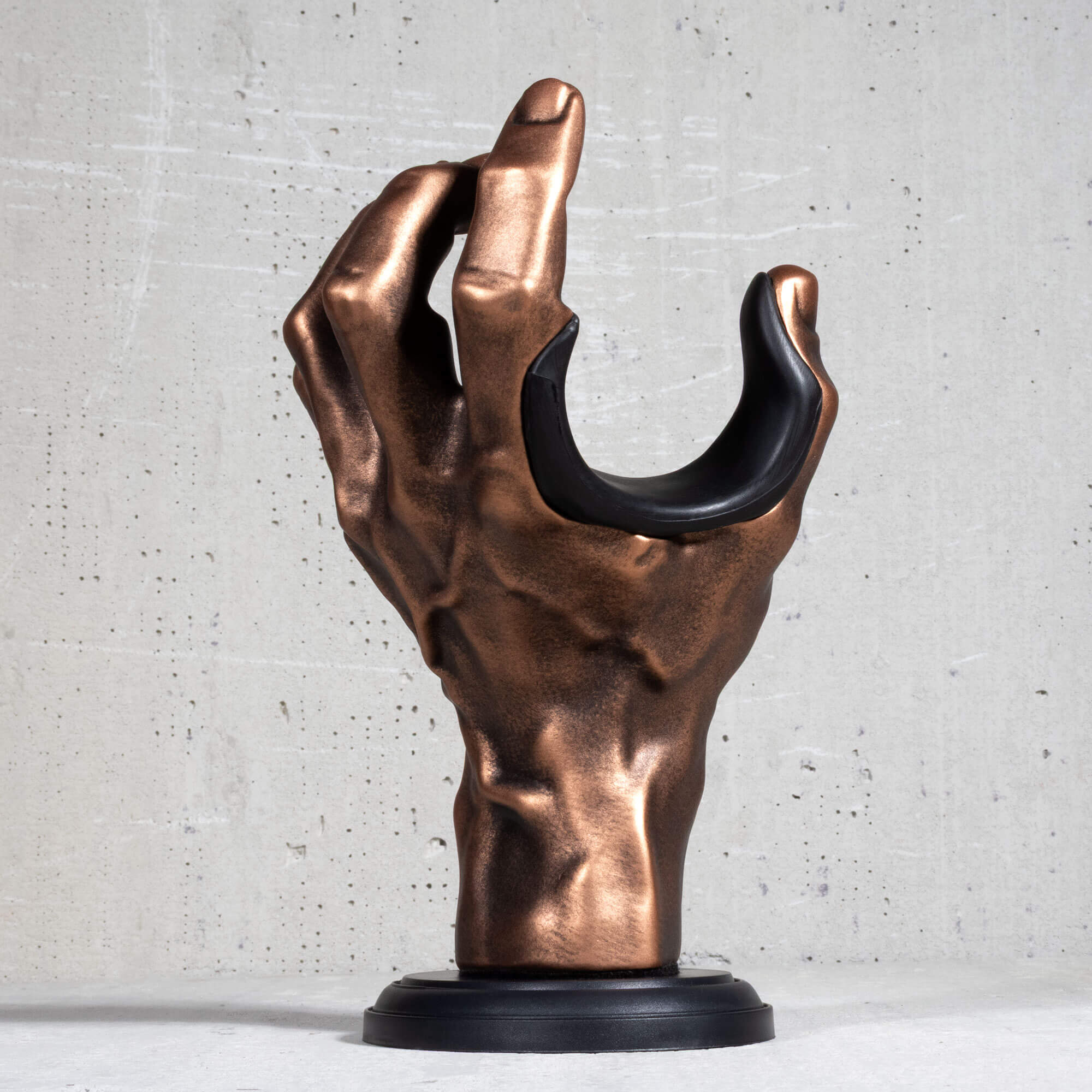 Copper hand guitar wall hanger with black pad on grey background.