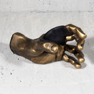 GuitarGrip gold hand sculpture guitar wall hook on a concrete surface.
