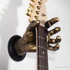 Bronze hand holding a guitar on a gray background.