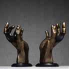 Gold hand sculptures on black bases against a gray background.