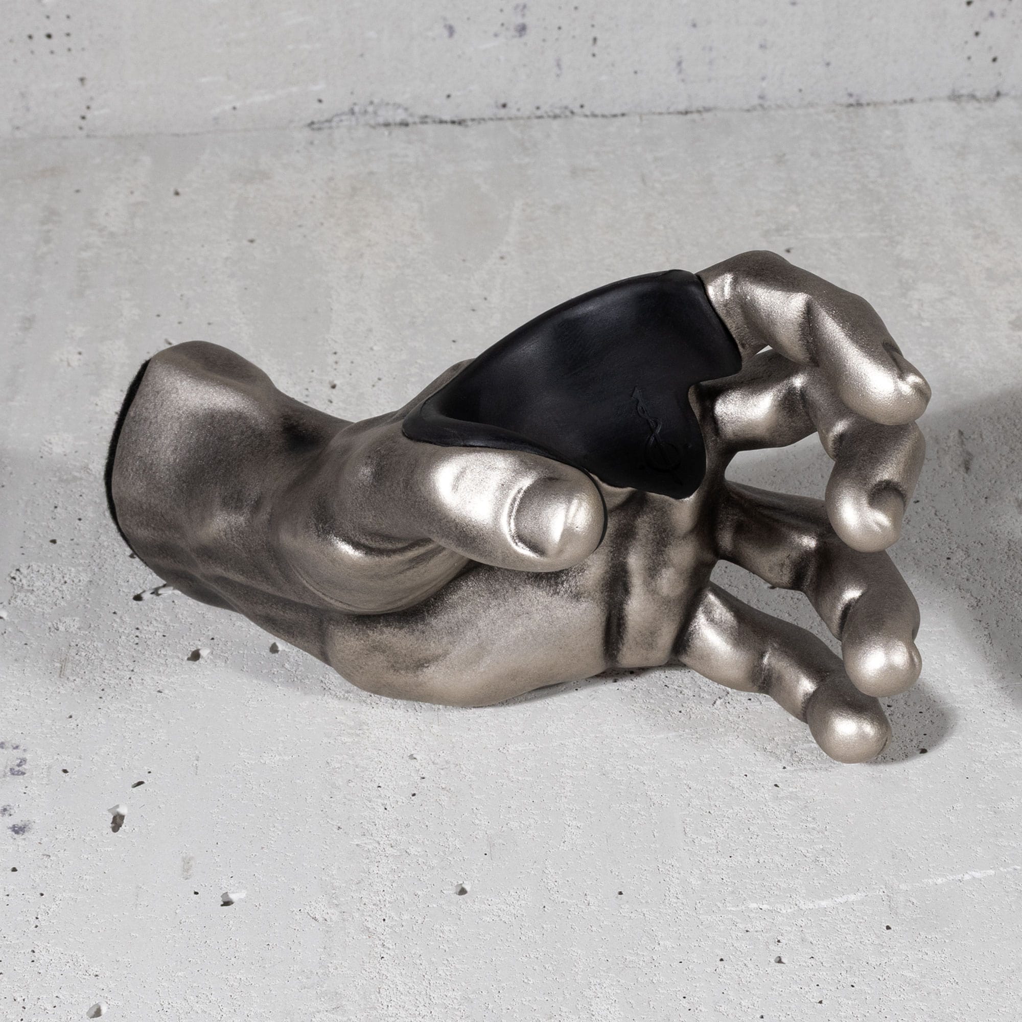GuitarGrip silver metallic hand with black padded insert on a concrete surface.

