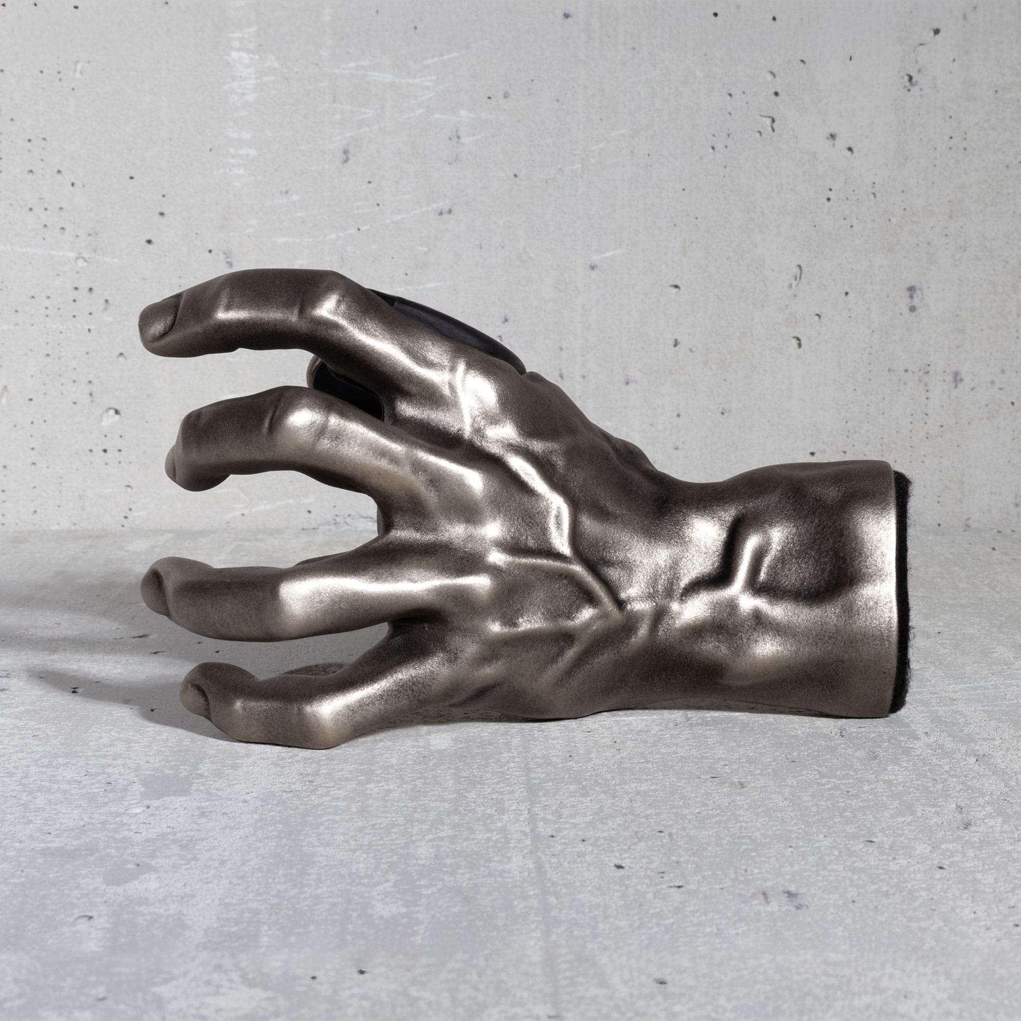 GuitarGrip guitar hanger metallic hand sculpture on a gray concrete surface.

