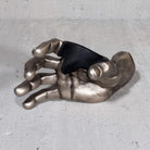 Metallic hand sculpture guitar hanger on a gray surface.

