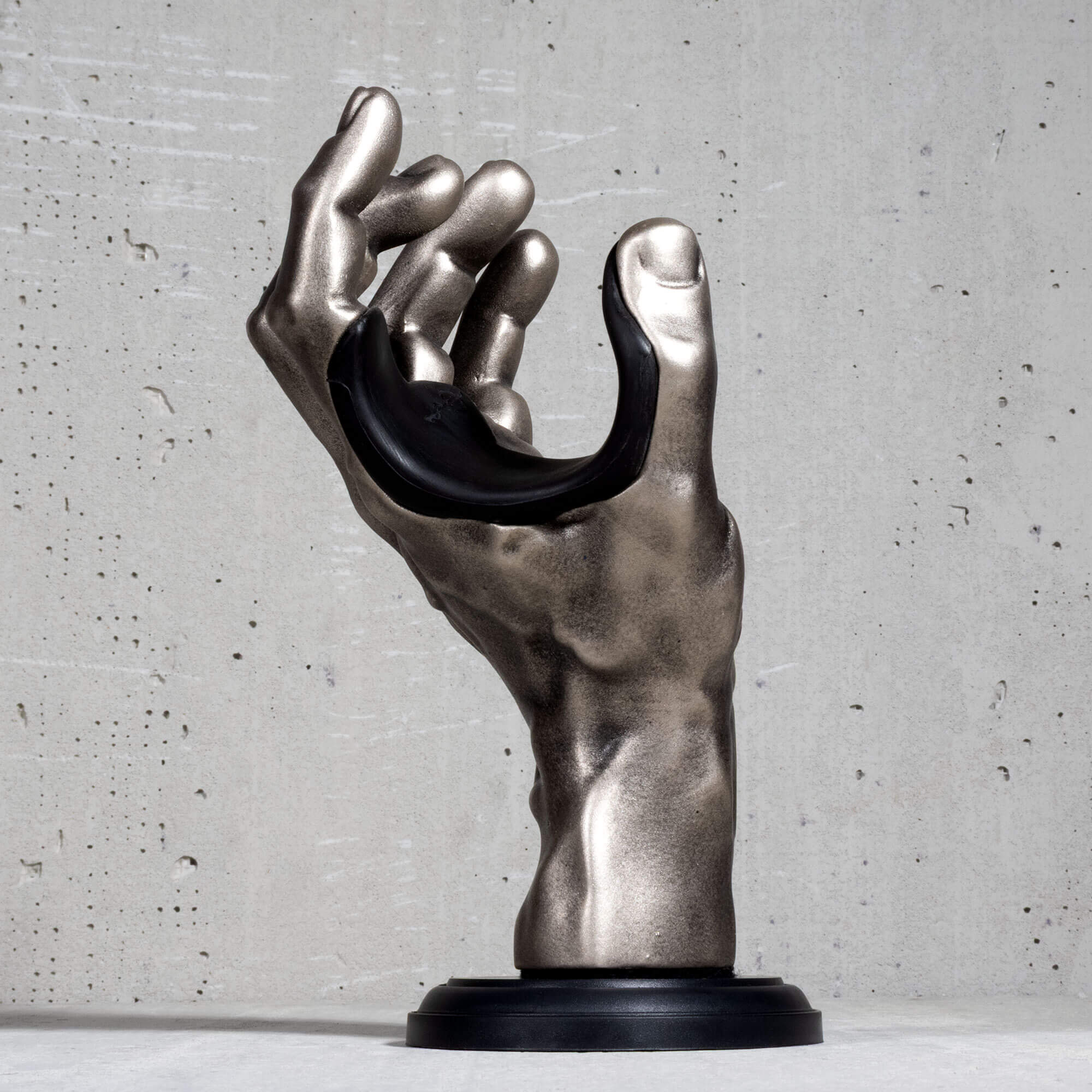 Hand guitar hanger wall mount in silver color on grey concrete backdrop.