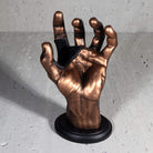 Copper hand guitar hanger with black disc on grey background.