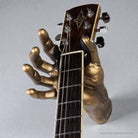 GuitarGrip gold hand guitar wall hanger with acoustic Alvarez guitar on grey wall.